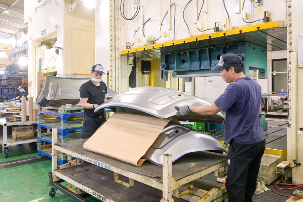 プレス機から加工された製品を取り出す社員二名